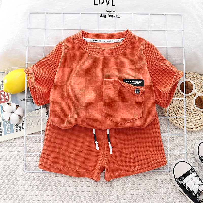 An orange boys' summer cotton t-shirt and shorts set laid out on a white surface.