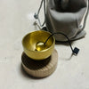 A small brass singing bowl rests on a wooden base with a black cord attached.