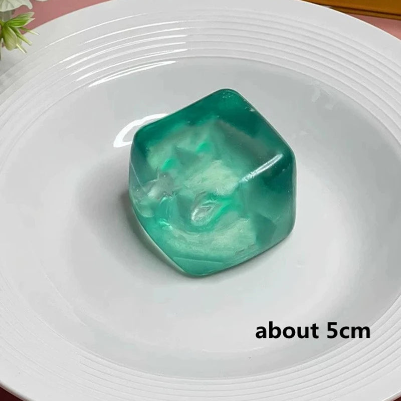 A translucent teal green ice cube sensory fidget toy resting on a white plate.