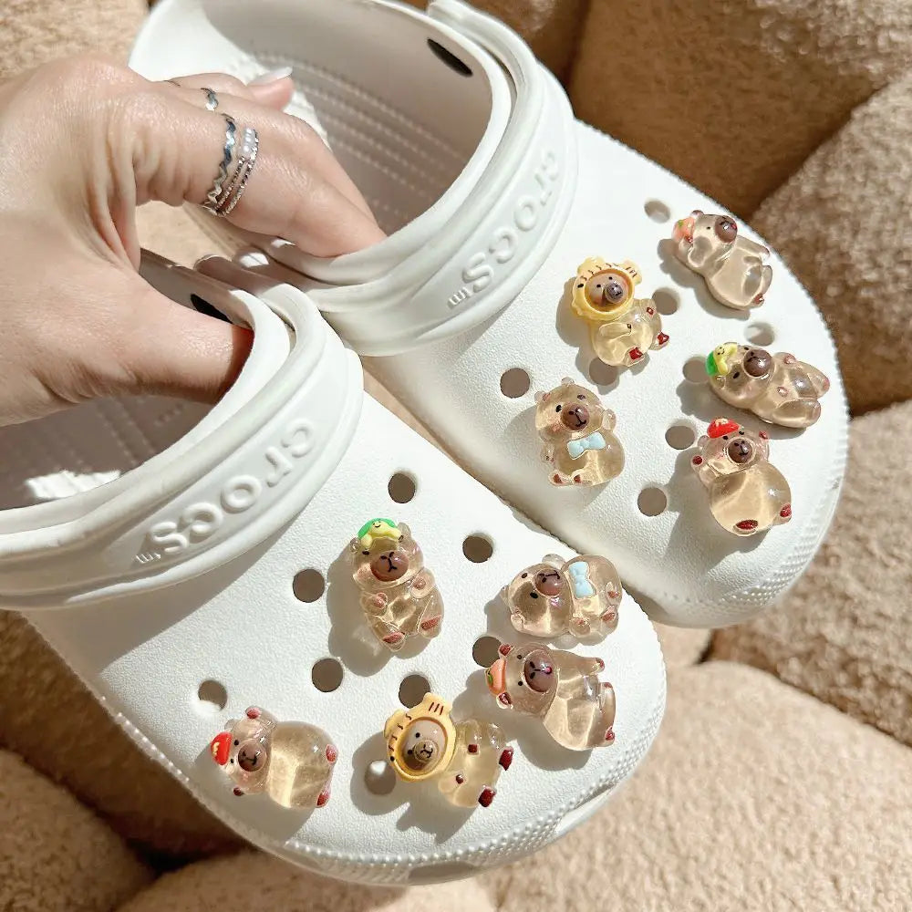 A pair of white Crocs shoes decorated with glow-in-the-dark capybara charms.