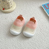 A pair of pink and cream breathable anti-slip baby first walker shoes resting on a white surface next to a wooden stacking to