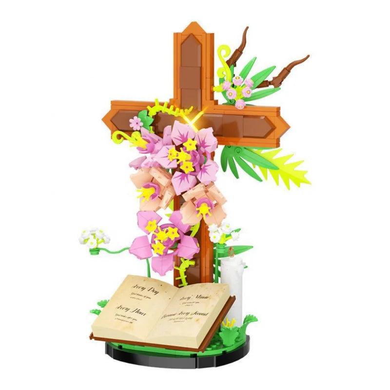 A religious Easter cross made of wooden building blocks decorated with pink and yellow flowers and green leaves.