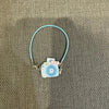 A light blue beaded necklace with a small camera doll charm on a gray fabric background.