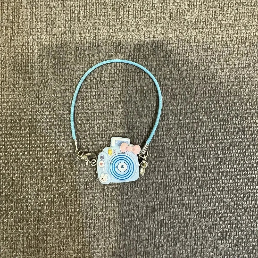 A light blue beaded necklace with a small camera doll charm on a gray fabric background.