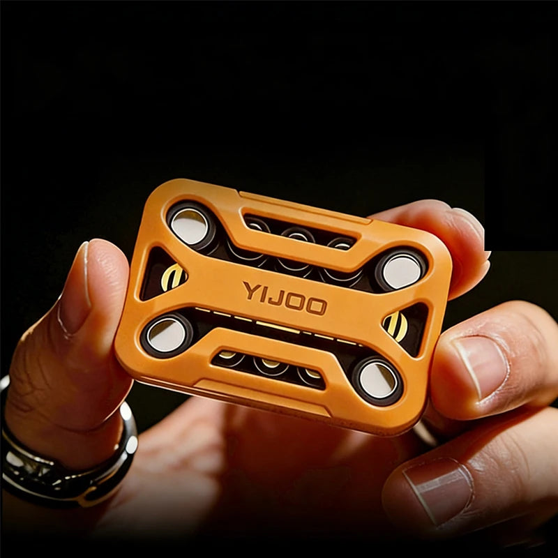 A hand holds an orange metal magnetic fidget slider with multiple rollers against a dark background.