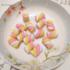 A collection of ten polymer clay marshmallow charms in pink and yellow stripes arranged on a white plate.