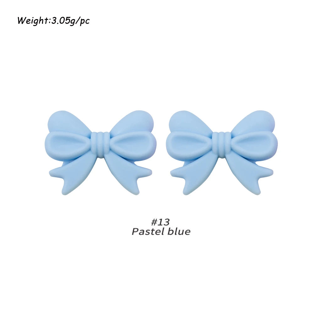 A pair of light blue silicone bow tie beads used for jewelry making and craft projects.