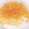 A pile of small, translucent orange glass rice beads for DIY jewelry and crafting.