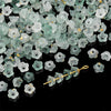 A pile of small, translucent green and clear bellflower acrylic beads for jewelry making.
