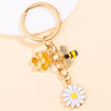 Gold-toned enamel keychain featuring a bee and a white daisy flower.