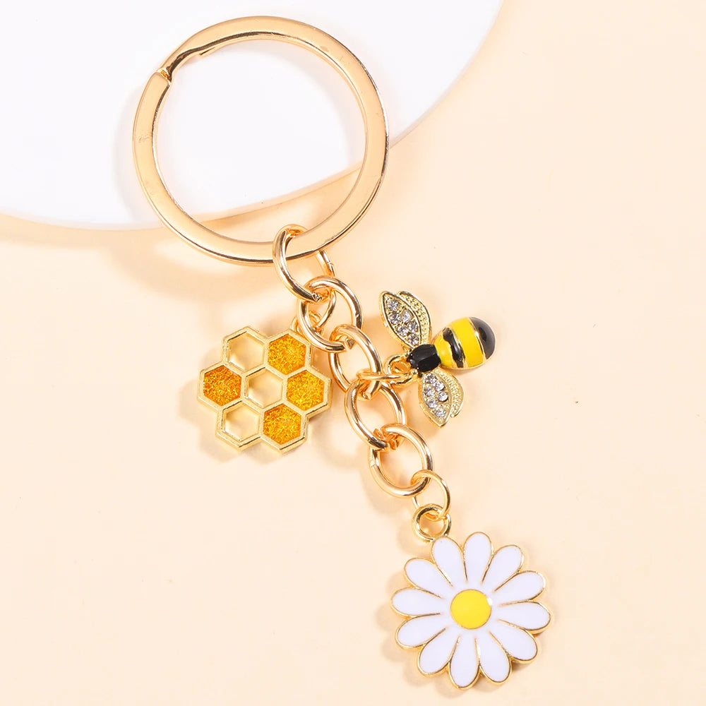 Gold-toned enamel keychain featuring a bee and a white daisy flower.