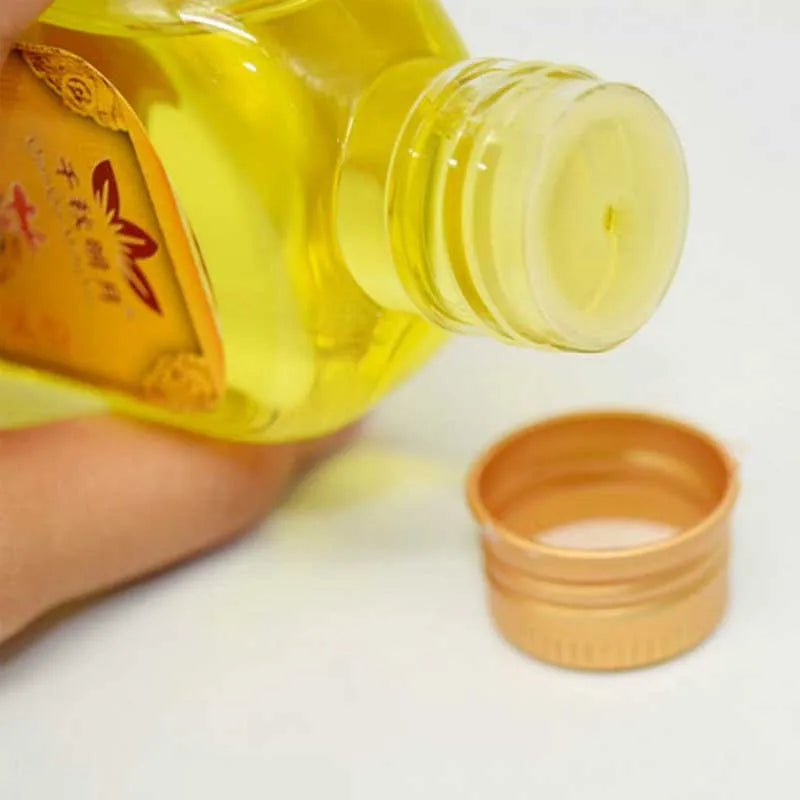 A hand holds a yellow glass bottle of Moxibustion Body Massage Oil next to an open copper oil dispenser.