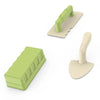 A green beach castle sand play set with a bucket and scoop resting on a light-colored surface.