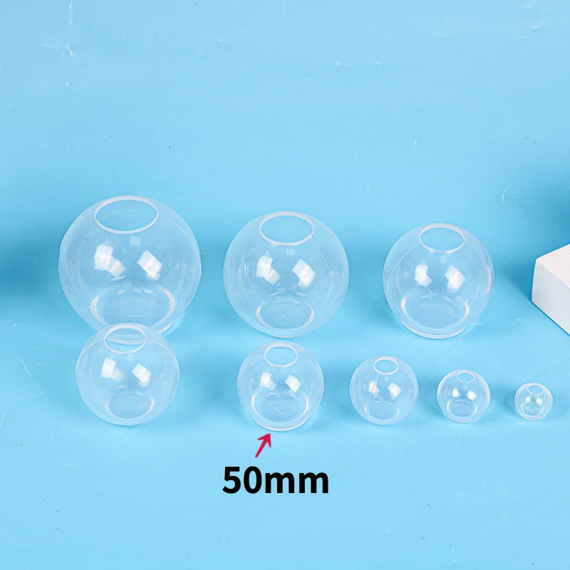 A collection of clear silicone sphere molds of various sizes, including a 50mm mold, displayed on a light blue surface.