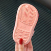 A pink lightweight children's clog with textured sole and size marking is held by a hand.