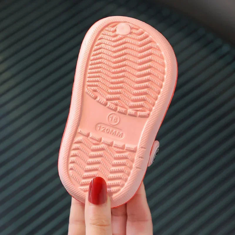 A pink lightweight children's clog with textured sole and size marking is held by a hand.