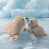 Two light brown seal plush toys sitting on ice with large blue icebergs in the background