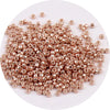A pile of small, round metallic glass beads in a rose gold color for jewelry making.