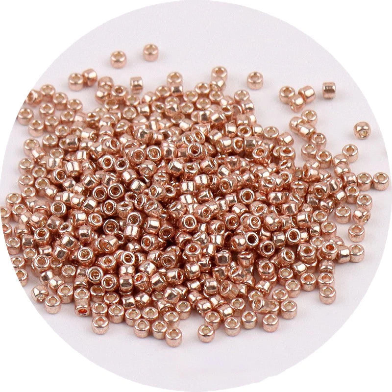 A pile of small, round metallic glass beads in a rose gold color for jewelry making.