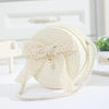 A cream-colored handwoven straw crossbody bag featuring a delicate white lace bow detail.