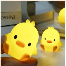 A hand holds a glowing yellow cartoon duck night light, illuminating a surface.