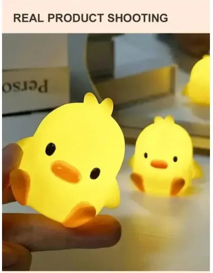 A hand holds a glowing yellow cartoon duck night light, illuminating a surface.