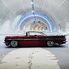 A red vintage 1959 Chevrolet Impala die-cast model car is displayed inside a futuristic, arched tunnel.
