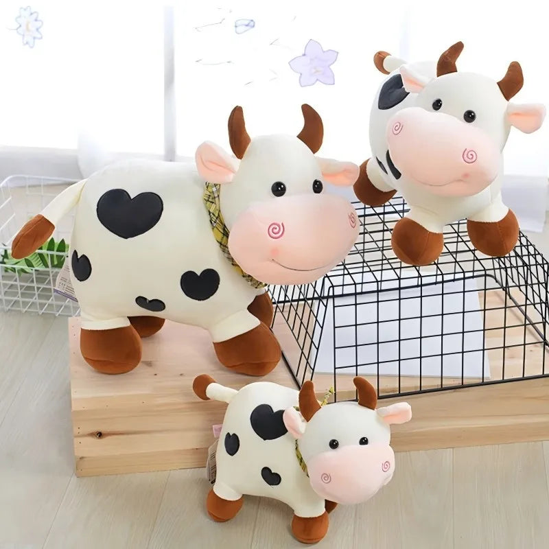 A set of adorable white and pink cow plush toys with black spots and soft features displayed on a wooden surface.