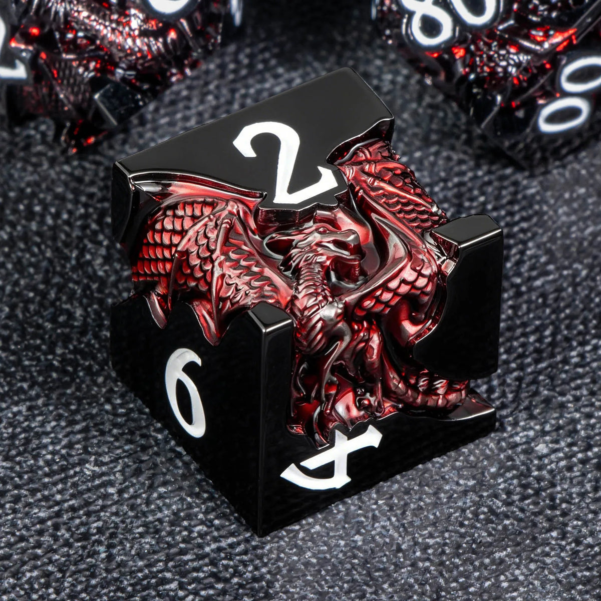 A black metal die featuring a red dragon design and the number 2, set against a dark gray background.