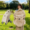 A woman is holding a beige baby windproof cape blanket with a dinosaur design in a grassy park setting.