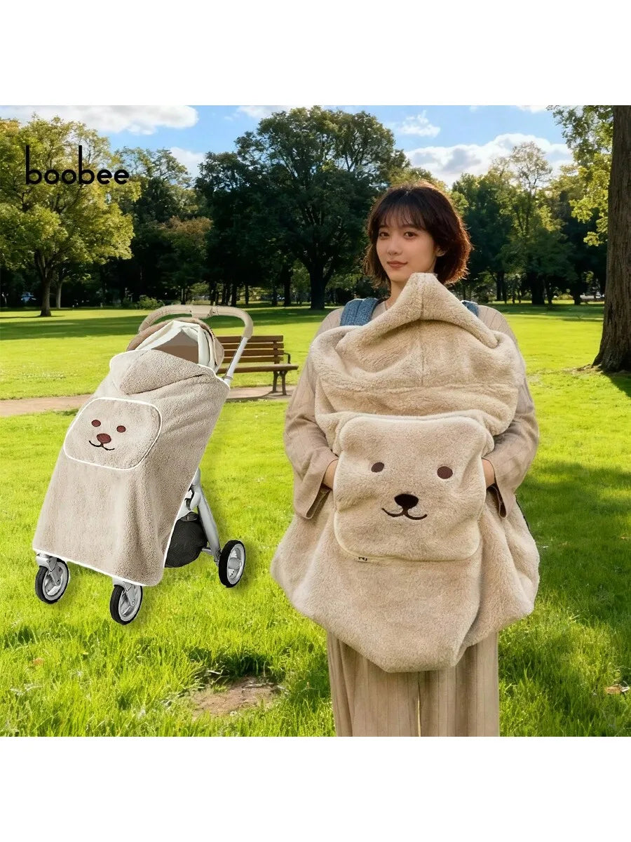 A woman is holding a beige baby windproof cape blanket with a dinosaur design in a grassy park setting.