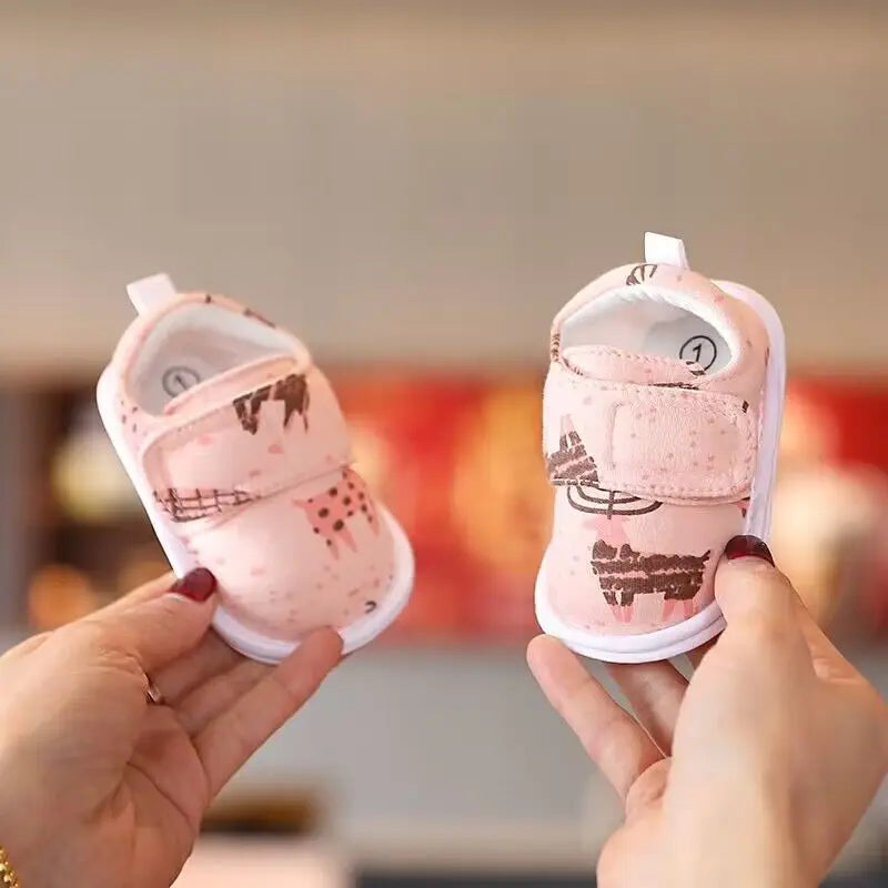 A pair of pink bear soft sole first walker shoes for babies being held by a person.