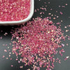 Crushed pink and magenta crystal glass mix for resin and jewelry making scattered on a dark surface.