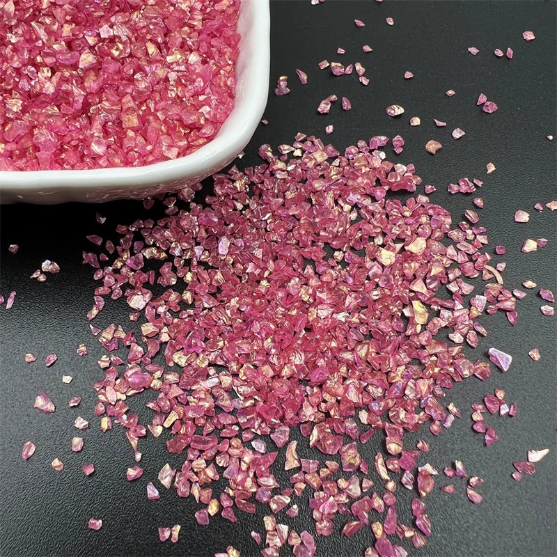 Crushed pink and magenta crystal glass mix for resin and jewelry making scattered on a dark surface.