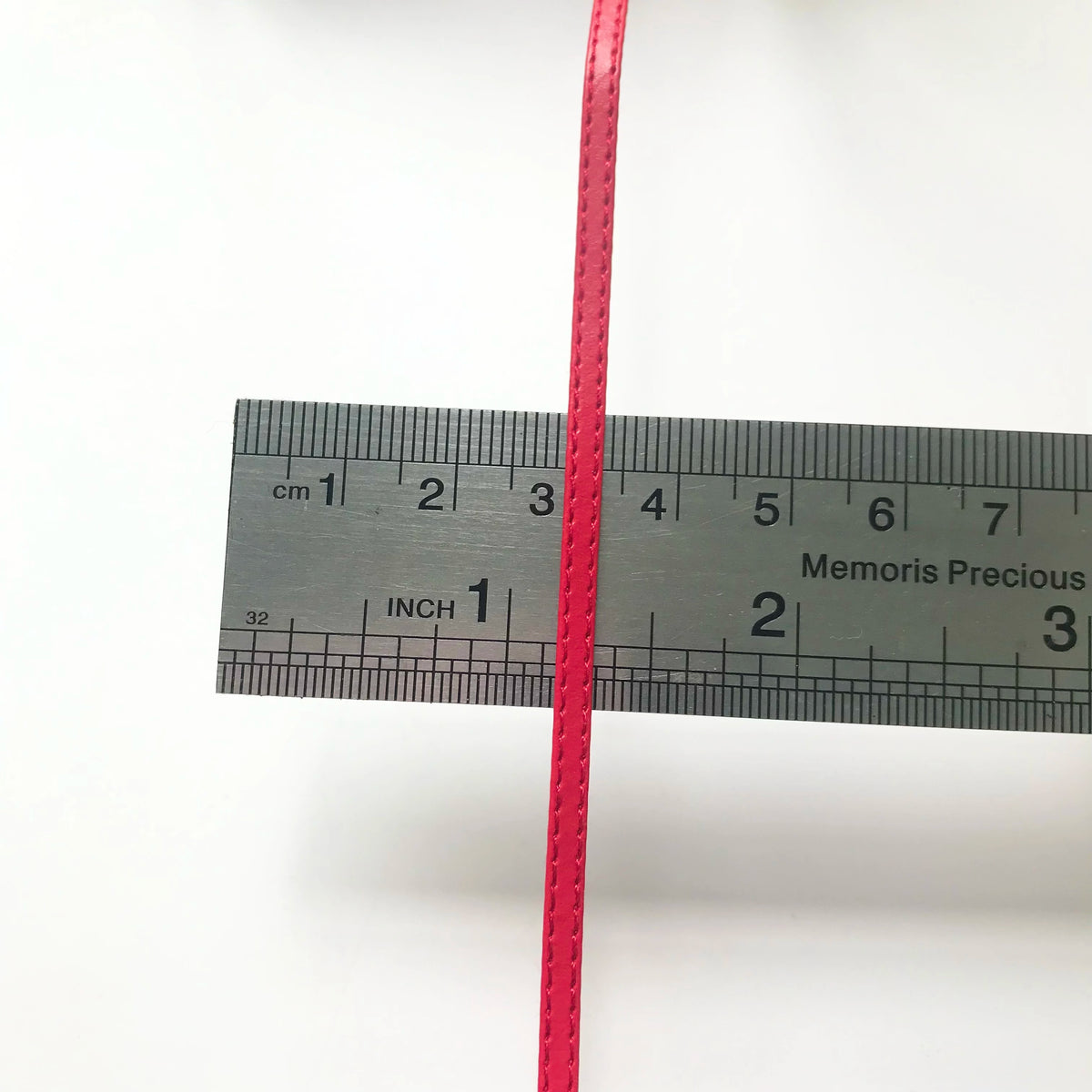 Nahaufnahme eines leuchtend pinken Bandes neben einem schwarzen Lineal mit Zentimetern und Zollmarkierungen.