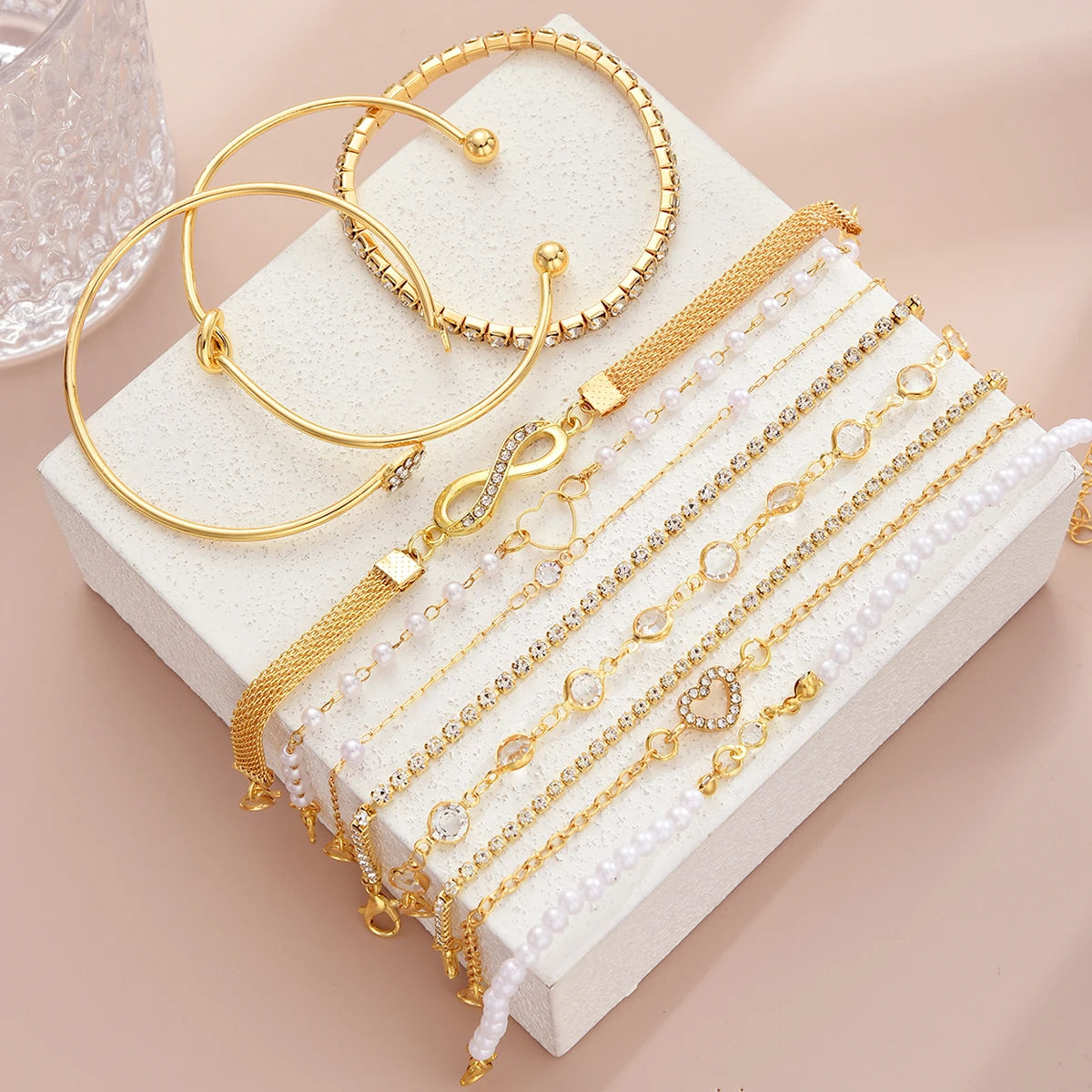 A collection of 11 gold and pearl bracelets featuring crystal hearts and infinity signs displayed on a white box.