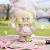 A fluffy pink and yellow plush keychain of a character with large eyes, set against a soft pink checkered background.