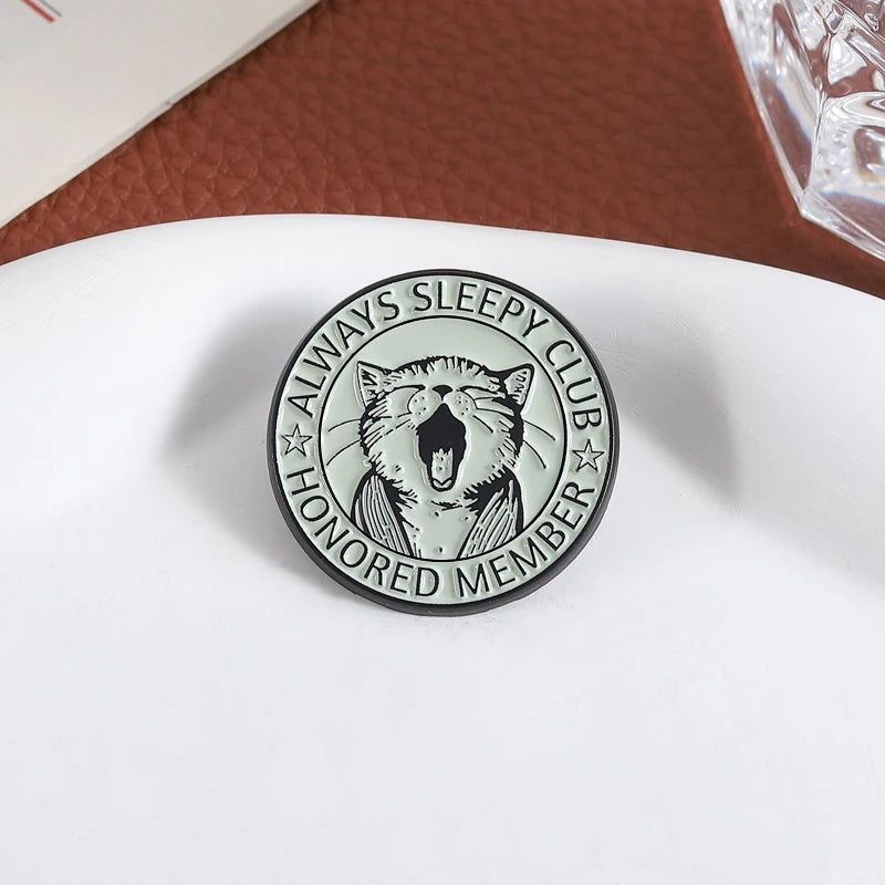 An enamel pin featuring a stylized, roaring cat face surrounded by the text Always Sleepy Club Honored Member