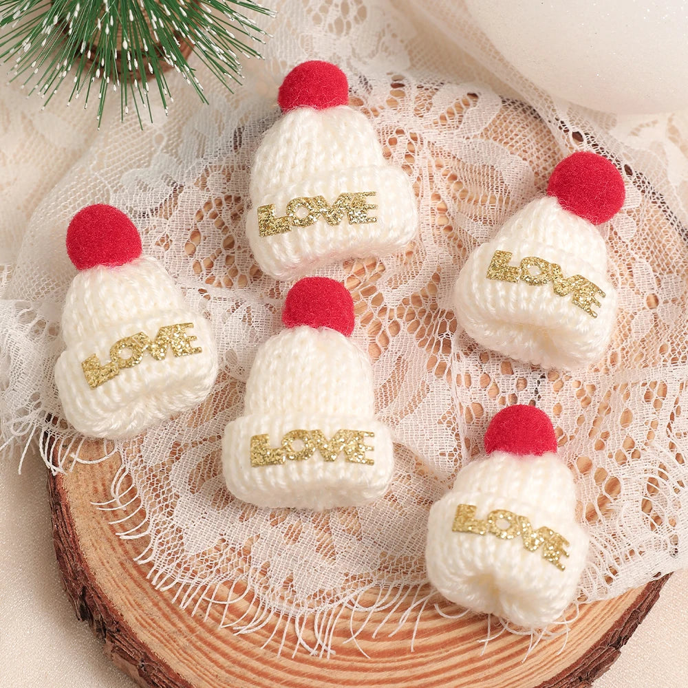 A set of mini knitted white hats with red pom-poms and gold lettering for Christmas doll dress-up accessories