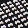 A close-up view of small, iridescent white and pink acrylic bow beads scattered on a dark surface.