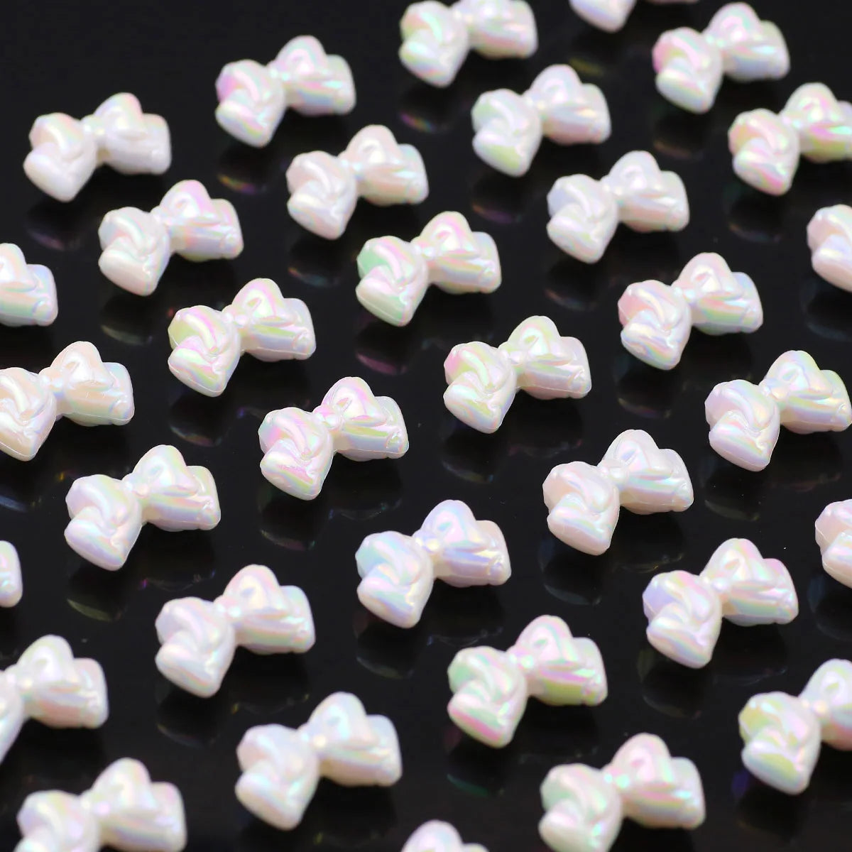 A close-up view of small, iridescent white and pink acrylic bow beads scattered on a dark surface.