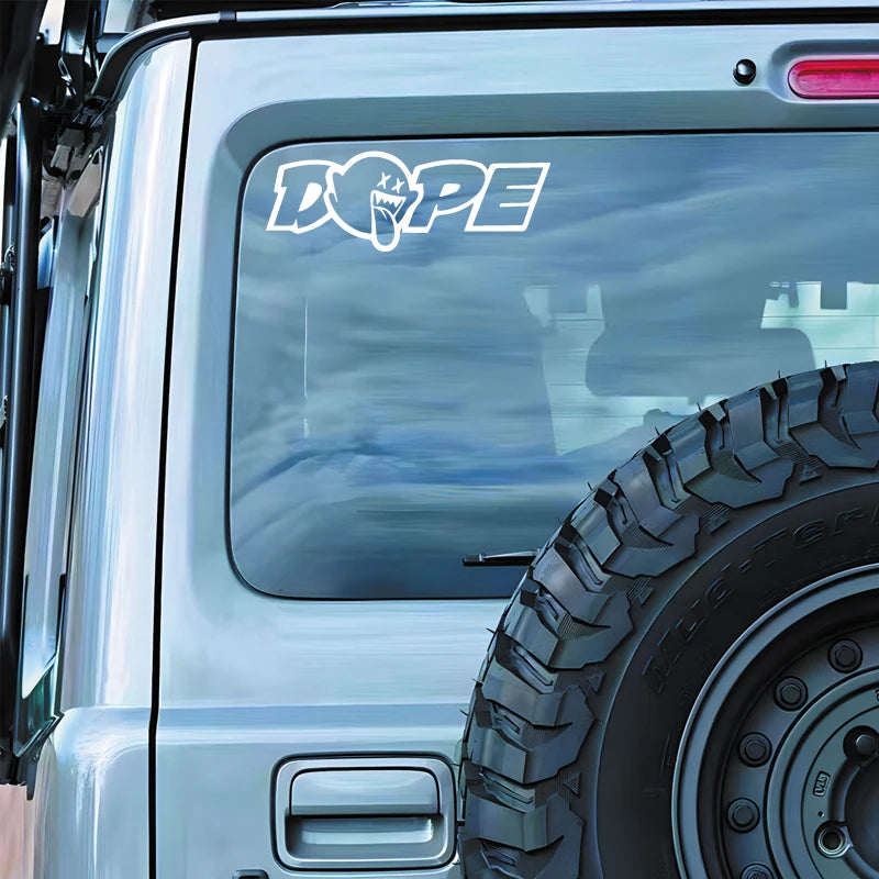 Close-up of a silver truck body with a DOPE decal sticker and a large off-road tire.