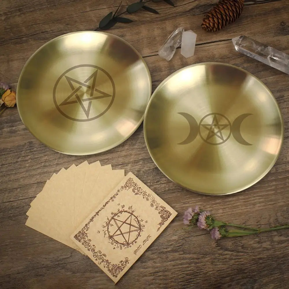 A brass pentagram altar plate rests on wood next to ritual parchment and pine cones.