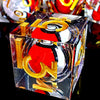 A clear resin die with a red and black dragon eye design and gold numbers, resting on a reflective surface.