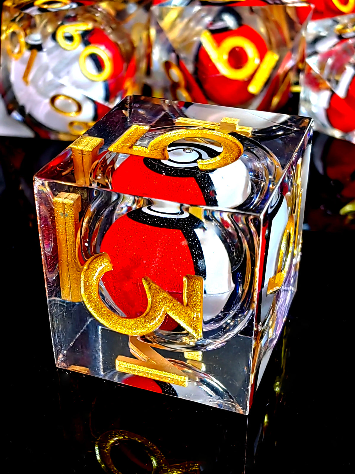 A clear resin die with a red and black dragon eye design and gold numbers, resting on a reflective surface.
