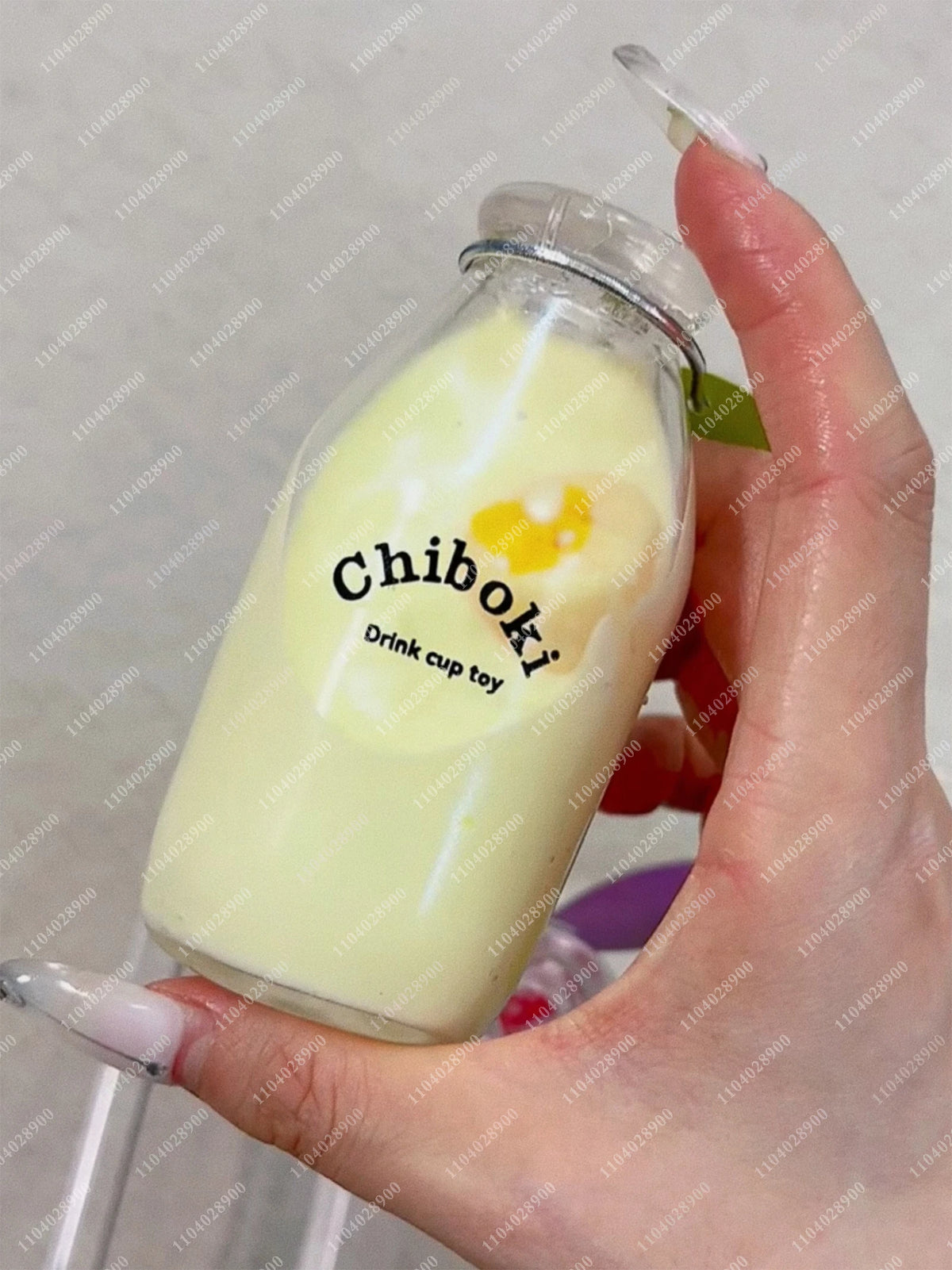 A hand holds a clear glass bottle filled with yellow liquid and a yellow squishy toy labeled Chiboki.
