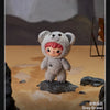 A small grey bear plush doll standing on a rock in a desert-like setting.