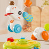 A white cartoon baby rattle toy with orange ears and blue accents is shown in a playful context.