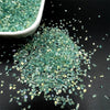 Crushed green glass crystals scattered on a dark surface with a small white bowl nearby.