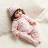 A pink baby doll wearing a matching pink romper and hat, lying on a white fluffy surface.